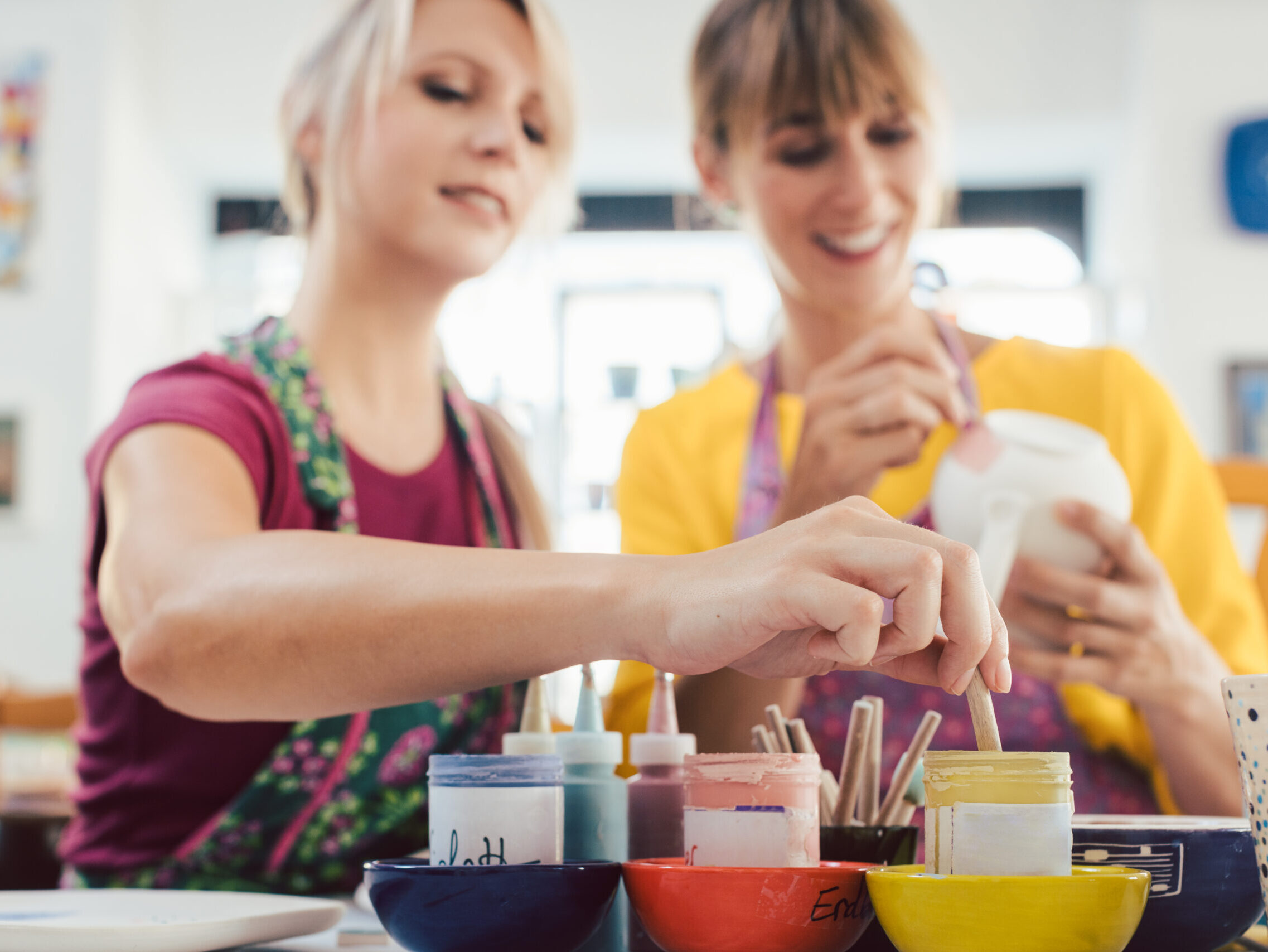 Two girl friends painting their own handmade ceramics in a hobby workshop